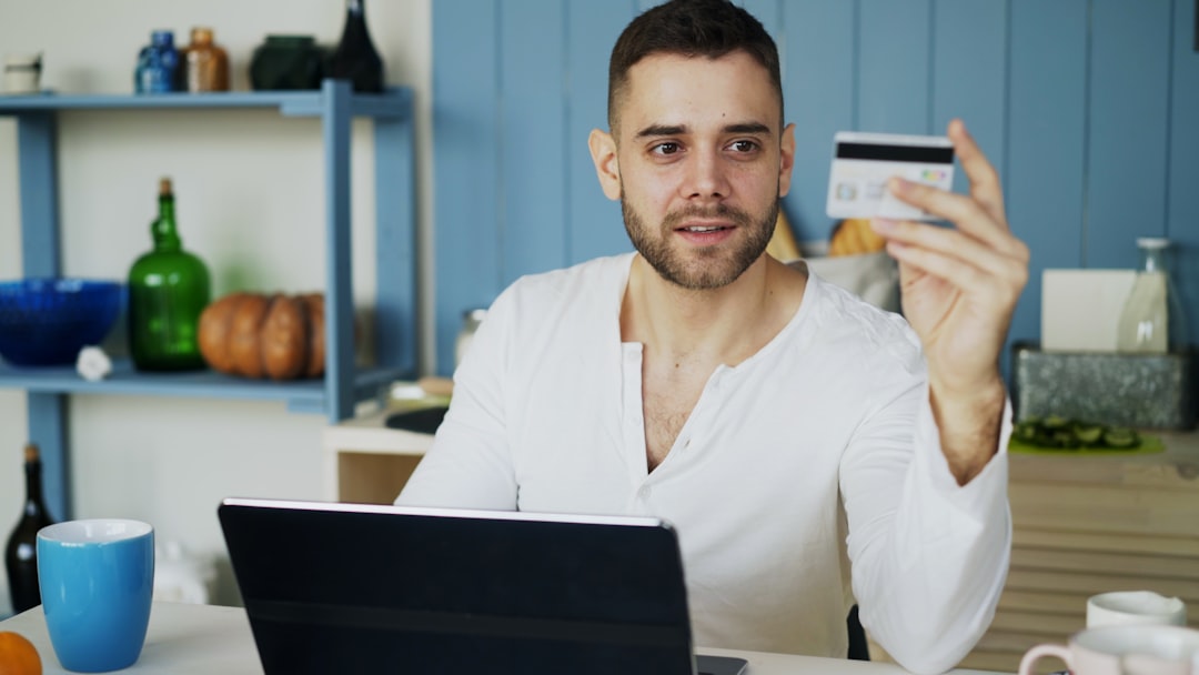 Young man having online shopping using credit card and laptop computer while have breakfast in the kitchen at home in the morning